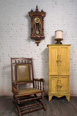 Wall Mural - Interior shot of retro wooden rocking chair, yellow cupboard and pendulum clock in on background of white bricks wall and parquet wooden floor