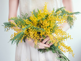 Bouquet of bright, yellow flowers in the hands of a young woman in a white dress. Wedding preparations