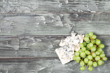 Pieces of blue cheese and green grapes on a wooden table. Copyspace for text.