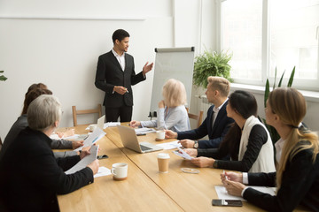 Poster - African businessman ceo boss in suit presenting corporate plan on flip chart at group meeting, black business coach leader giving presentation explaining team goals in conference room at training