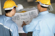 Blueprint in architect's hand. Blur foreground are architect  and engineer in yellow helmet ,they are planning on blueprint.