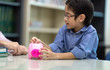 © Nattanon - Father teaching his son about saving money.  Kid with a Pink Saving Pig Jar in the Library. Setup studio shooting. selective focus at coin in hand.