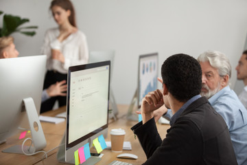 Focused african manager discussing project with senior colleague at workplace, serious multiracial young and old team coworkers talking about work sitting in front of computers, teamwork concept