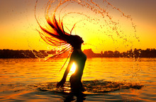 Beauty Model Girl Splashing Water With Her Hair. Girl Silhouette Over Sunset Sky. Swimming And Splashing On Summer Beach Over Sunset