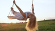 LENS FLARE CLOSE UP: Happy young woman smiles and leans back on swing in nature