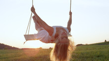 LENS FLARE, CLOSE UP: Attractive young woman leans back on swing while swaying.