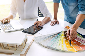 Poster - Two young women interior design or graphic designer working on project of architecture drawing with work tools and color swatches, colour chart in digital tablet at workplace