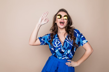 Wall Mural - Beautiful cheerful summer young woman in sunglasses standing over a color background