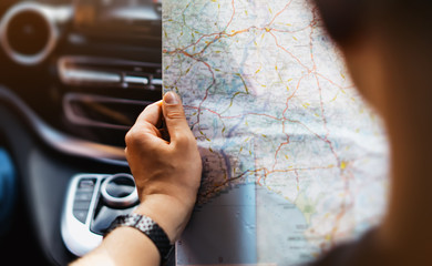 Hipster man holding in male hands and looking on navigation map in auto, tourist traveler hiker driving on background panoramic view way road, trip in transportation, person sitting in auto