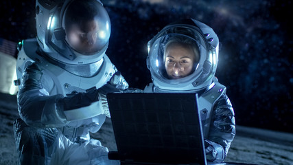 Wall Mural - two astronauts wearing space suits work on a laptop, exploring newly discovered planet, communicatin