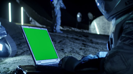 Wall Mural - astronaut on the alien planet works on a mock-up green screen laptop. in the background her crew mem
