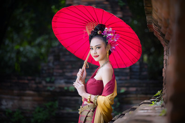 Beautiful Thai girl in traditional dress costume red umbrella as Thai temple where is the public place, Thai Woman in Traditional Costume of Thailand.