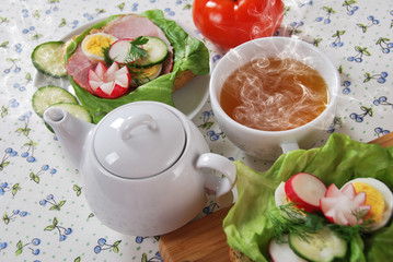 white kettle hot sweet fruit tea with two sandwiches with cucumber ham and green salad