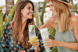 © WHstudio Leushin N - Pretty brunette woman clinks cocktail with her best female friend, meet together after summer holidays, share positive impressions. Relaxed lesbian couple spend free time in terrace cafeteria