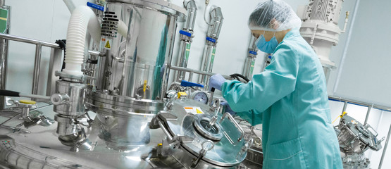 Pharmaceutical factory woman worker in protective clothing operating production line in sterile environment