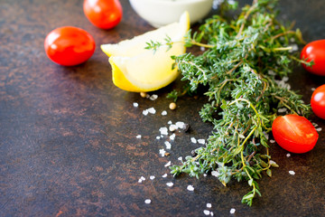 Wall Mural - Ingredients for cooking on a dark stone table - thyme, cherry tomato, olive oil and lemon.