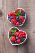 Berries fresh mix in heart shaped ceramic jars overhead on wooden table background in studio