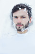 © Yulia - Authentic art close up portrait of handsome Caucasian bearded man lying on snow while having solo camping trip. Winter gear walking along fast flowing rocky river, in scenic outdoor nature destination