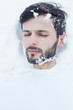 © Yulia - Interesting authentic shot of brunette handsome man in white t-shirt lying on white pure snow surface closing eyes, suffering from freezing, got lost in mountains during his vacation trip for skiing