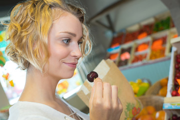 attractive young grocery clerk tasting cherry in grocery store