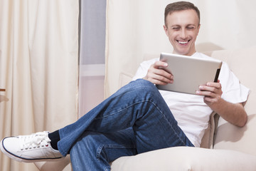 Youth Ideas and Concepts.Portrait of  Happy Smiling Caucasian Man with Tablet Computer on Couch. Posing on Couch in Home Environment