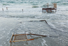 Beautiful Sea Landscape. Surf Azure Waves Break On A Small Metal Red Pier, Forming A Foam And A Splash