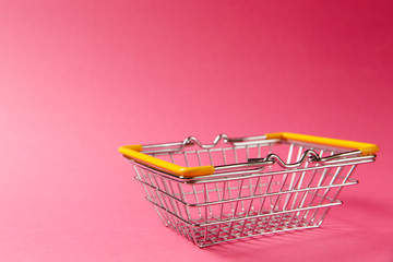 Wall Mural - Close up of metal grocery basket for shopping in supermarket with lowered handles and yellow plastic elements isolated on pink background. Concept of shopping. Copy space for advertisement