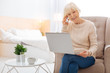 © Viacheslav Yakobchuk - Progressive pensioner. Smart positive excited pensioner feeling happy while sitting in a nice comfortable bedroom and talking on the phone while looking at the screen of a convenient modern laptop