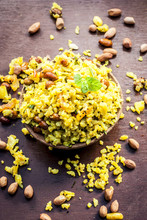 Close Up Of Indian Popular Brunch Dish In A Clay Bowl With Dried Fried Groundnut On It Is Poha Batata Or Pava Batata On A Wooden Surface In Dark Gothic Colors.