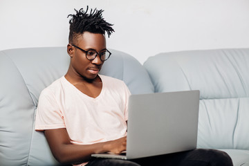 Wall Mural - African American man sitting with laptop on sofa