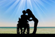 Silhouette of a disabled man in a wheelchair and his wife who is kissing by the sea