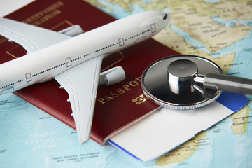 Boarding pass and a passport travel documents with medical stethoscope and airplane on world map background, close-up. Medical travel concept