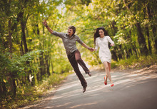 Young Boy And Girl Are Running Along The Road And Jumping Up Fun. The Newlyweds Laugh Happily. Hooray Concept.