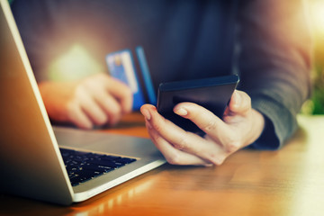 Online payment,Young Man's hands holding smartphone and using credit card and computer laptop for online shopping.