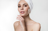 Fototapeta Zachód słońca - Portrait of calm young woman is touching her skin with satisfaction. She is standing while wearing towel on head. Isolated