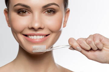 Close up portrait of joyful girl brushing her teeth with enjoyment. She is looking at camera and smiling. Isolated