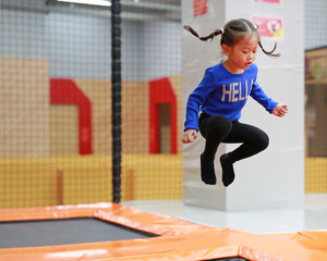 Wall Mural - Asian kid girl jumping at trampoline in indoors playground. Active girl having fun at sport center on holiday.