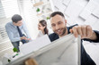 © Viacheslav Yakobchuk - Office work. Attractive content young bearded employee smiling and holding a sheet of paper and his colleagues working in the background