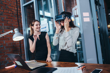 Two female application developers testing a new app designed for VR headset standing in modern office