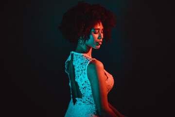 Wall Mural - Beautiful black woman with curly hair showing her naked back, wearing a white dress in a studio in front of a dark background