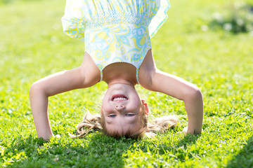 happy little kid girl standing on her head on green lawn.
