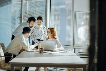 Feedback needed. Upbeat young colleagues being gathered around their boss with a laptop and watching a presentation of their new project together