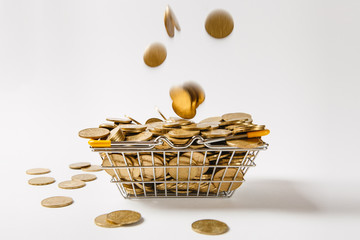 Wall Mural - Metal grocery basket for shopping in supermarket with lowered yellow handles with the coins falling into it isolated on white background. Concept of shopping, money. Copy space for advertisement