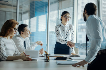 Business etiquette. Charming young businesswoman shaking hands with her male colleague while having a meeting with the other partners