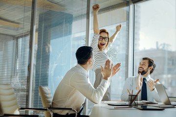 Poster - Perfect birthday. Upbeat young woman raising her hands and laughing happily celebrating her birthday while her colleagues clapping their hands and congratulating her