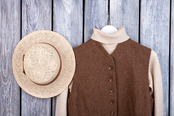 Wall Mural - Straw brim hat and wool sweater in sleeveless jacket. Flat lay, top view. Grey desk surface background.