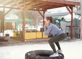 Wall Mural - Young muscular woman training on heavy tire, outdoors