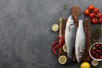 Fresh raw seabass on cutting board with ingredients. Top view, copyspace.