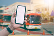 Hand man holding smartphone with blank white screen on blur image of bus station  background