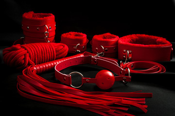 Sexual kink, erotic games and human sexuality concept with complete red sex toy kit set (ball gag, cuffs, rope, flogger, collar and leash) for BDSM fantasy play and bondge restraints on black silk